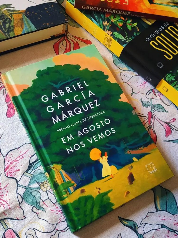 capa do livro em agosto nos vemos de gabriel garcia marquez em cima da cama e próximo a outros livros.