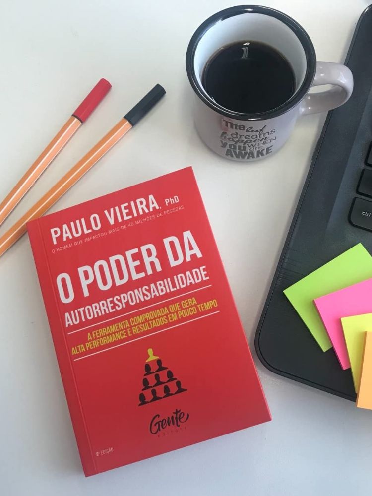 livro o poder da autorresponsabilidade de paulo vieira sobre a mesa, ao lado de notebook, caneca de café e canetas.